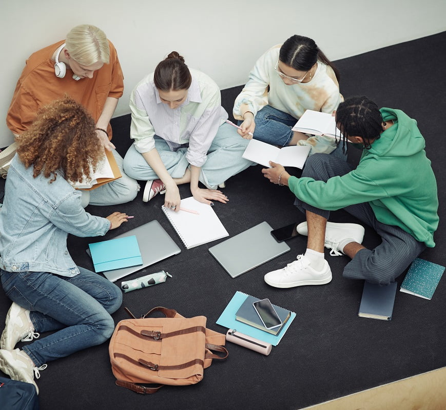 Above angle of group of multicultural teens in casualwear discussing notes Liceum Korczaka
